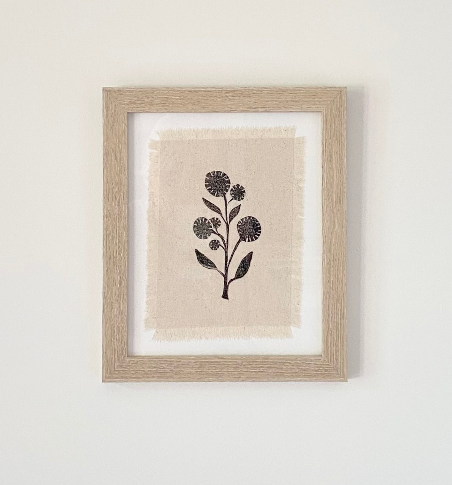 Framed block printed textile art. Black wildflower silhouette on off white cotton fabric with frayed edges.