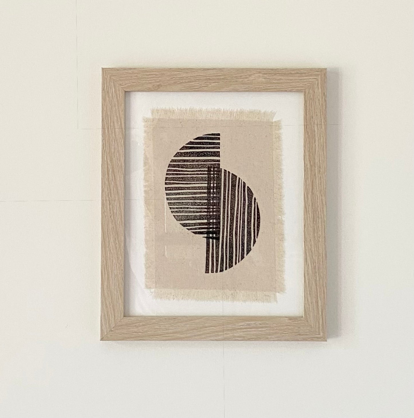 Block printed text in a frame.  Black half circles overlapping on off white frayed canvas.  Natural colored frame.