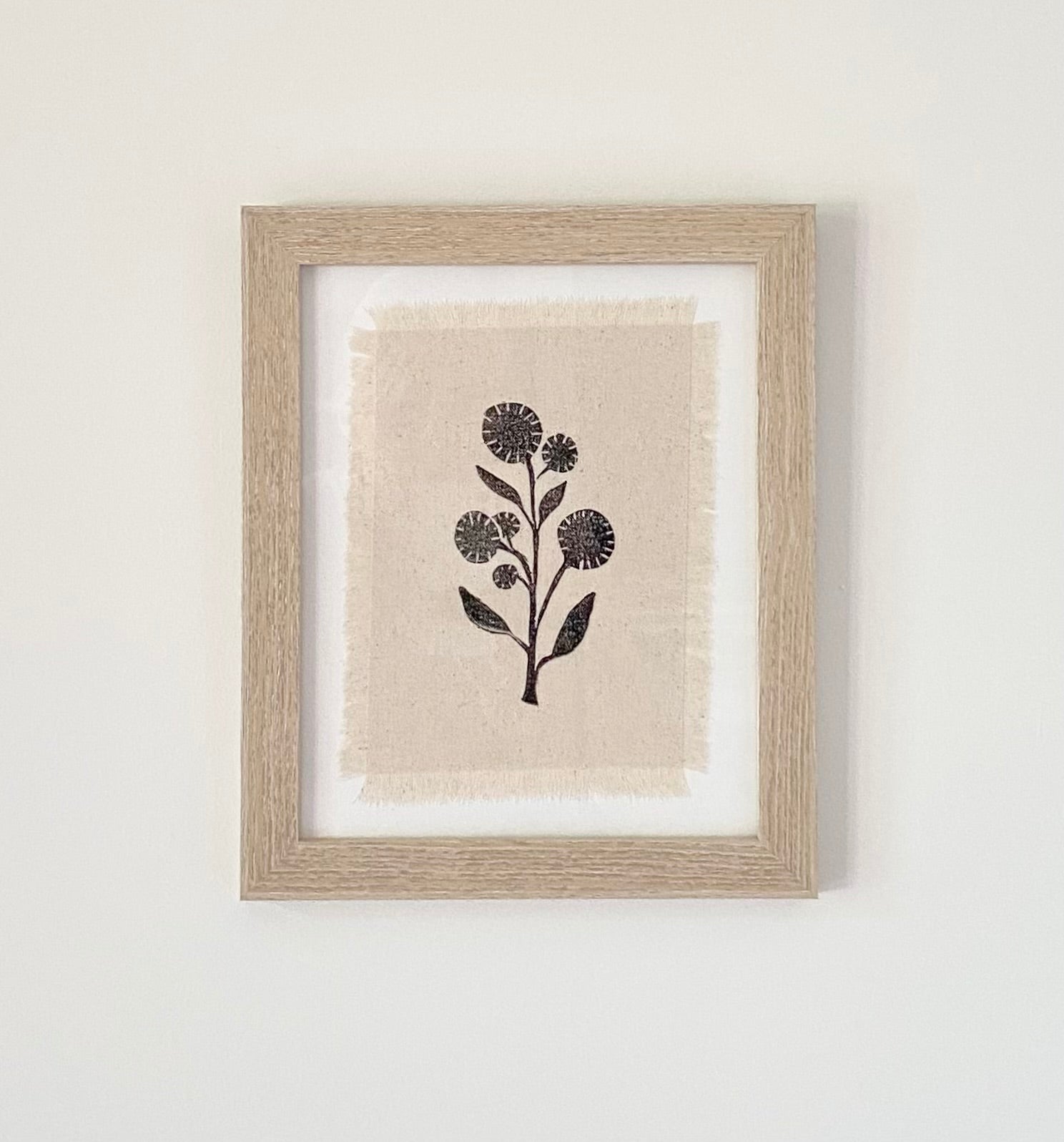 Framed block printed textile art. Black wildflower silhouette on off white cotton fabric with frayed edges.