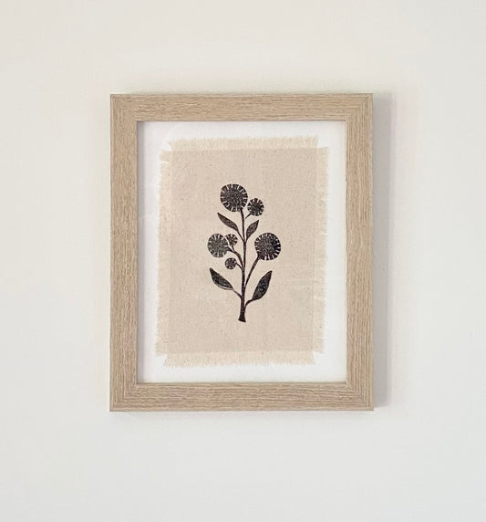 Framed block printed textile art. Black wildflower silhouette on off white cotton fabric with frayed edges.